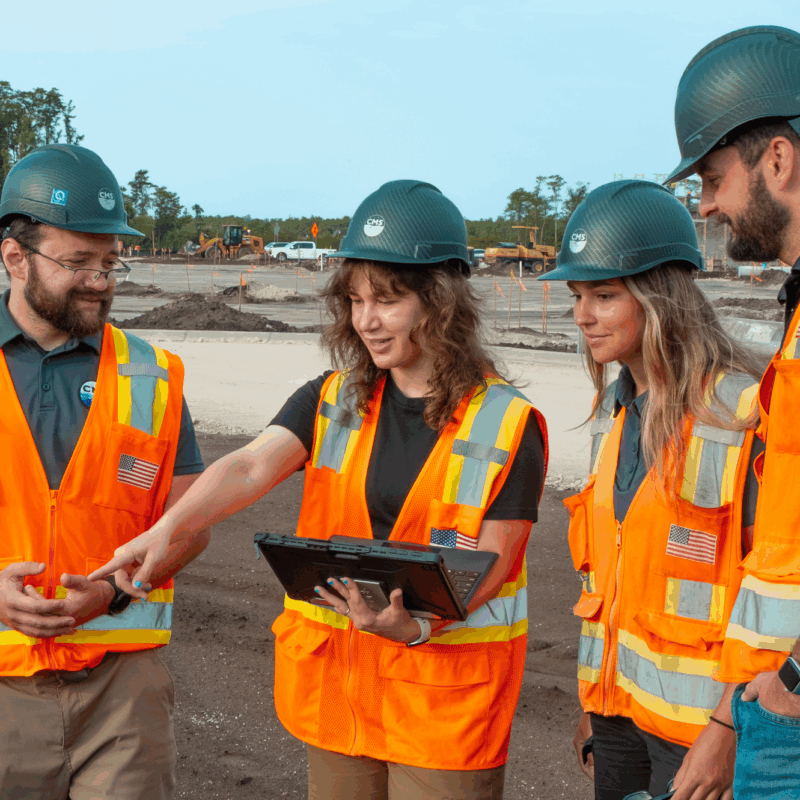 Four construction workers review plans on a tablet at site.