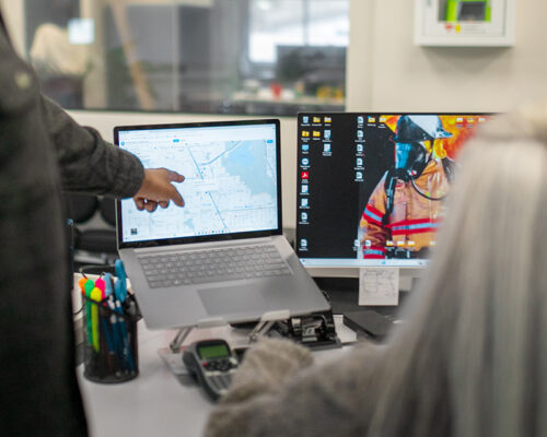 Two people at dual monitors, one points at a map.