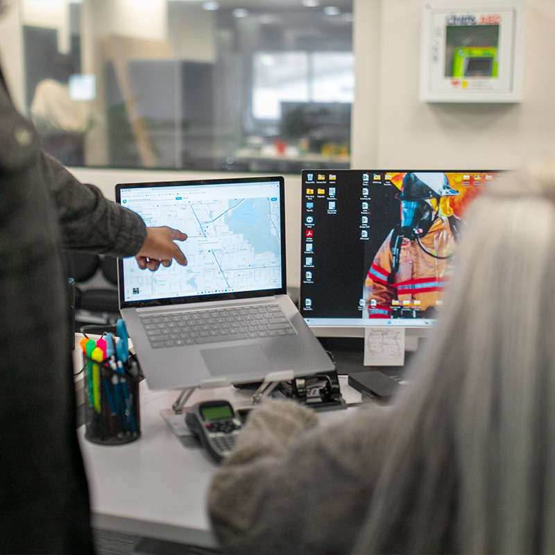 Two people at dual monitors, one points at a map.