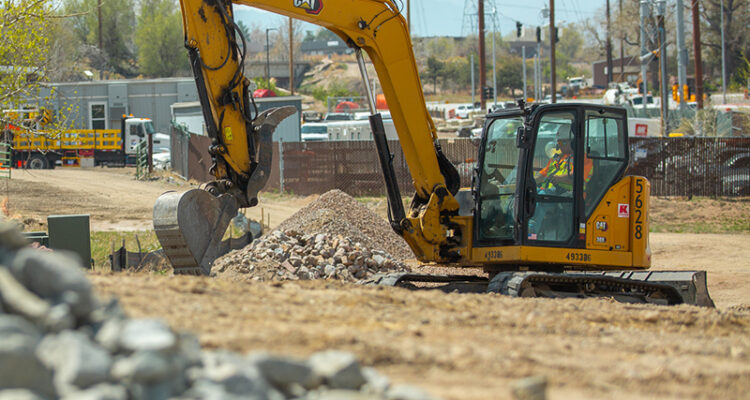 Yellow excavator moves rocks at construction site with vehicles.