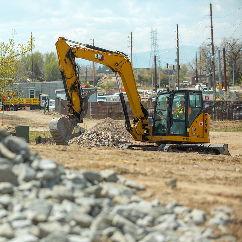 Yellow excavator moves rocks at construction site with vehicles.