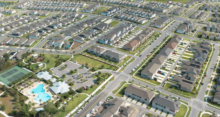 Suburban neighborhood aerial: houses, pool, tennis courts, construction.