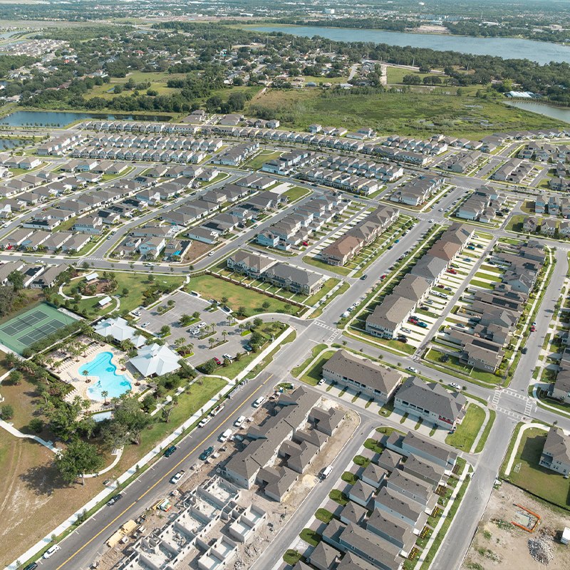 Suburban neighborhood aerial: houses, pool, tennis courts, construction.