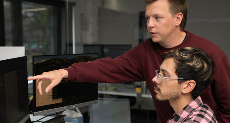 One person types as another points at a monitor.