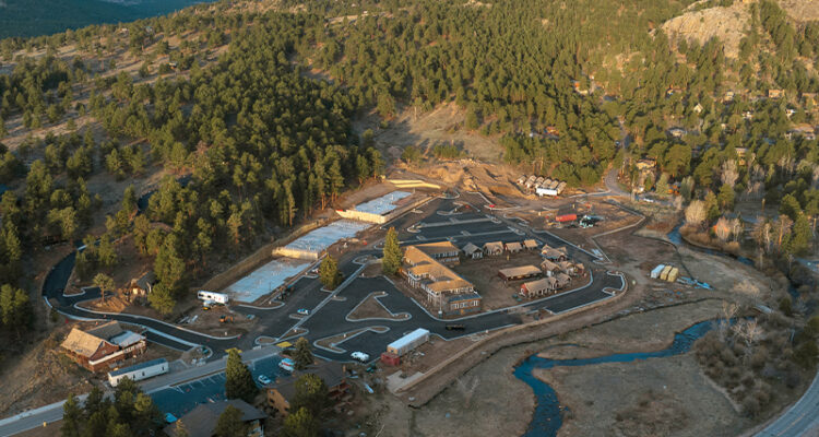 Aerial view of a small town, winding roads, creek, snowy peaks.