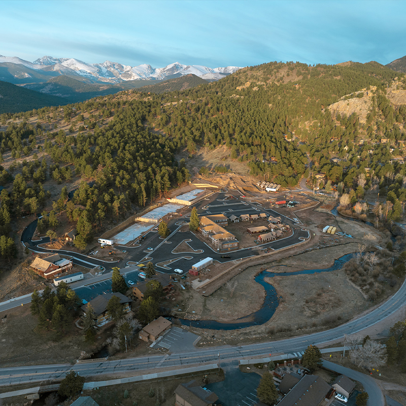 Aerial view of a small town, winding roads, creek, snowy peaks.