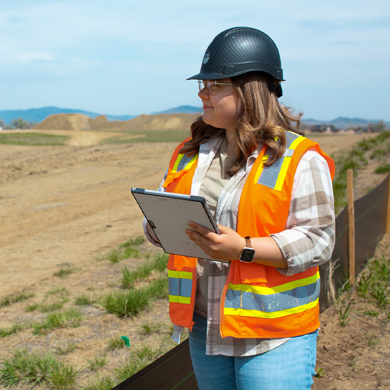 Worker in hard hat and vest holding clipboard on construction site.