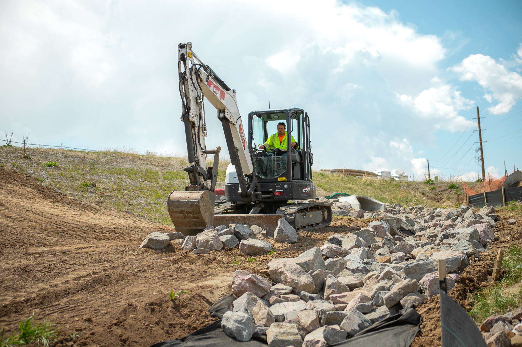 Worker in neon vest uses excavator to move rocks outdoors.