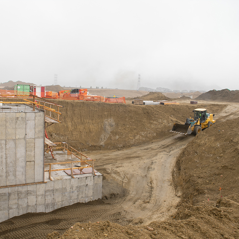 Bulldozer near dirt excavation and concrete foundation at site.