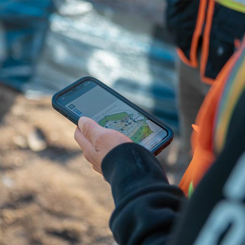 Person in safety vest holding phone with map at worksite.