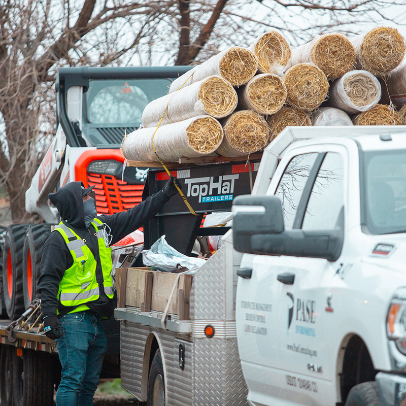 Worker in vest secures materials on flatbed trailer.