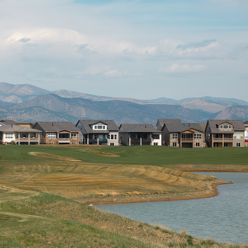 Modern houses, golf course, pond, mountains, partly cloudy sky.