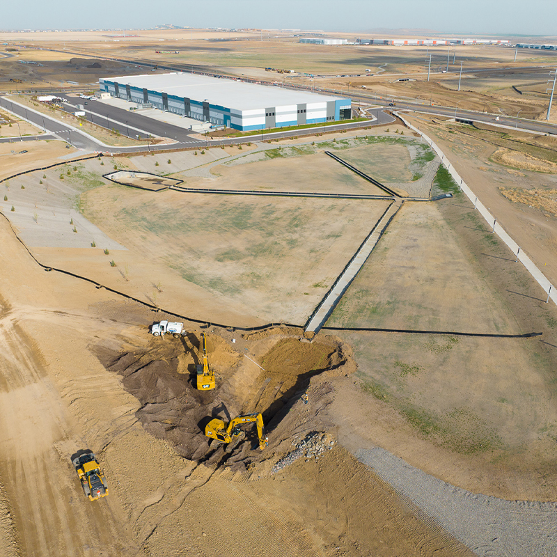 Aerial view: two excavators, dump truck, construction by warehouse.