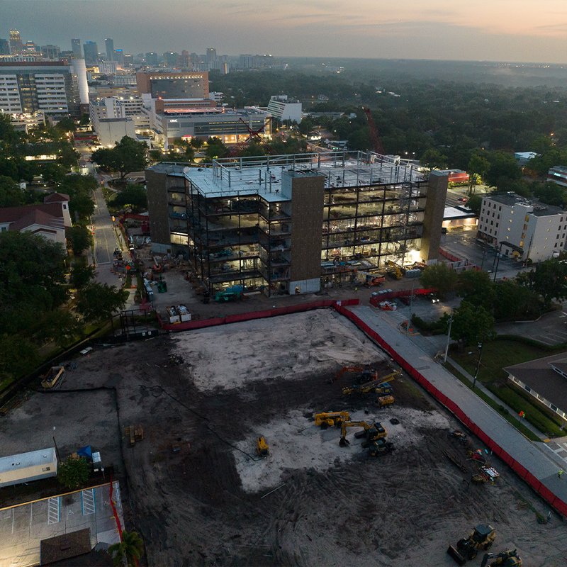 Aerial shot: unfinished building, cranes, city lights at dusk.