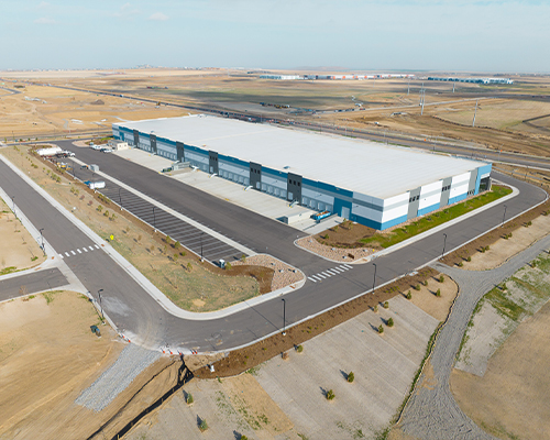 Aerial view of modern warehouse, parking lots, roads, fields.