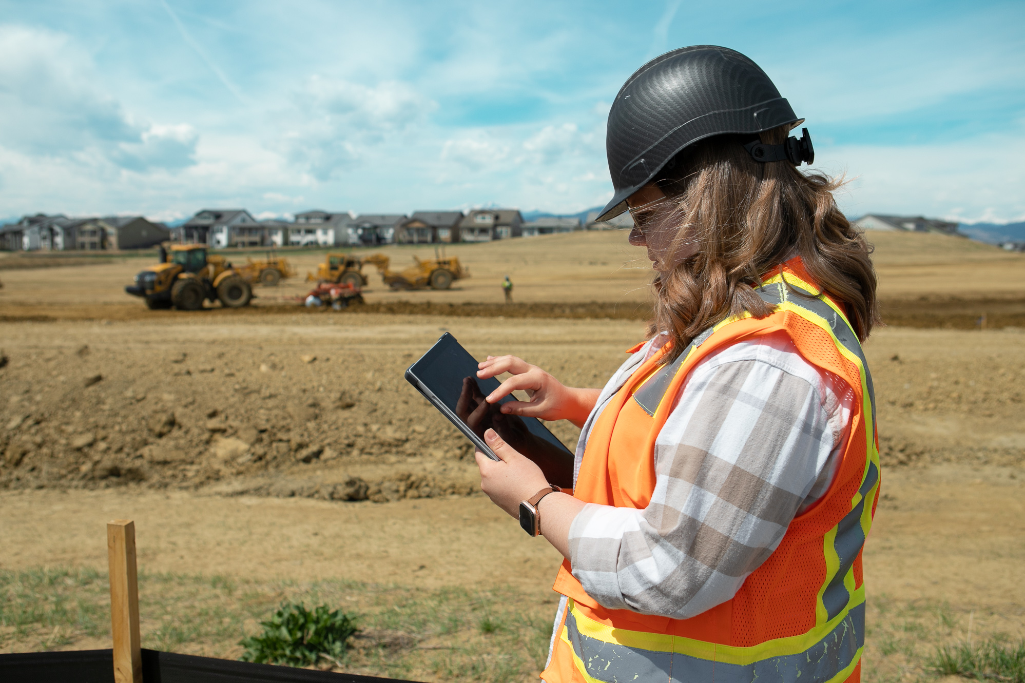 Person in hard hat and vest uses tablet at construction site.