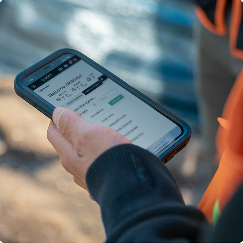 Person outdoors holding smartphone with project dashboard displayed.